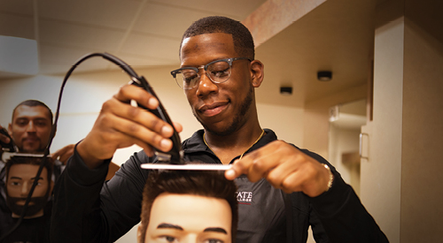 man trimming the hair of a manikin head using a comb and trimmer