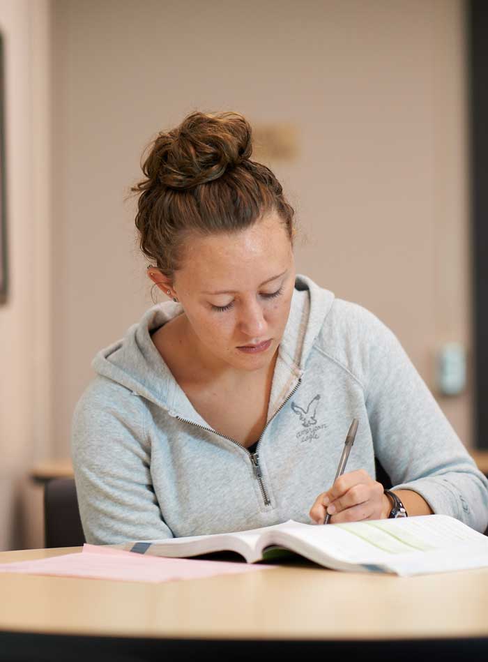 Woman studying and writing notes in college lounge.