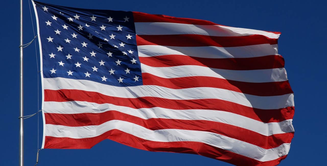 the flag of the united states of america, blue rectangle with 50 white stars in the upper left, 13 alternating red and white stripes horizontal everywhere else. Fluttering in a breeze.