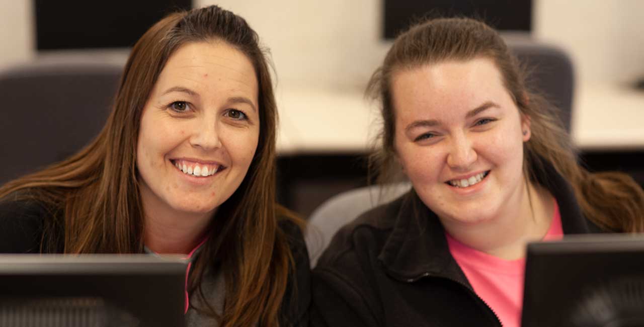 Two woman smiling at computers
