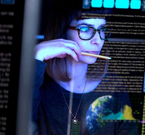 Female IT professional holding a pencil looks at a computer monitor displaying code and images