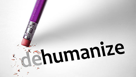 the word dehumanize is written on paper as an eraser from a pencil is in the process of erasing the "de"