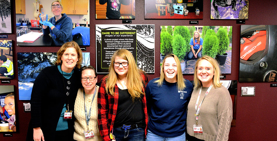 Mid-State staff members and students stand in front of Non-Traditional Occupation photo wall at Wisconsin Rapids Campus
