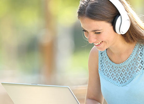 Woman sitting with headphones on looking at a laptop