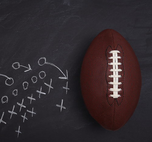 X's and O's drawn on black paper in the format of a play from a football playbook. A football is lying next to the drawing.