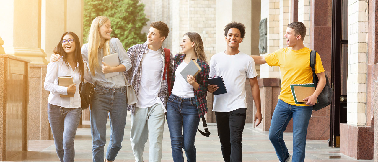 6 students walking together all carrying books smiling