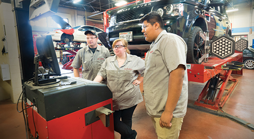 3 people standing in front of a computer with a land rover behind them looking at diagnostics pulled up on the screen