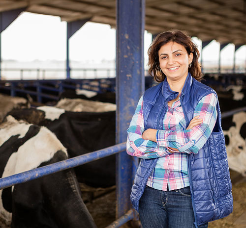 Woman standing with her arms crossed inside of an enclosure next to cows