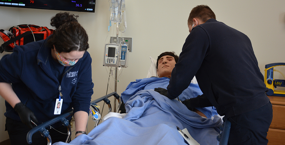 2 students working with a healthcare dummy on a gourney