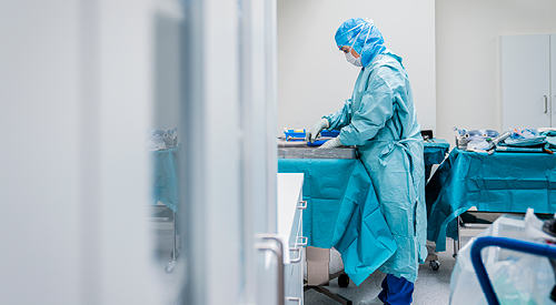 medical professional in full body and face coverings cleaning items in a pan