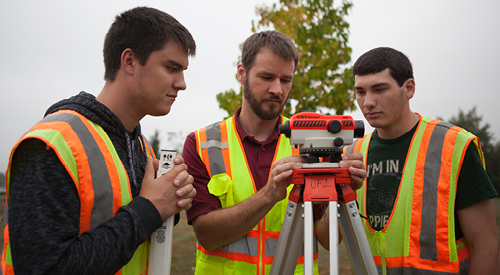 civil engineering students with an instructor looking at a piece of equipment wearing yellow and orange safety vests