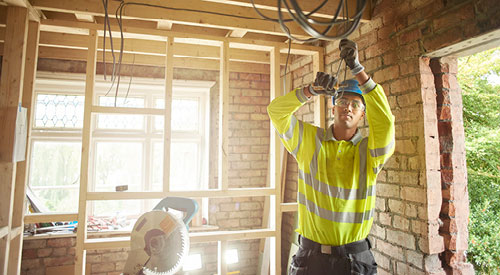 man working with electrical wiring wearing a safety had and glasses along with a bright orange shirt