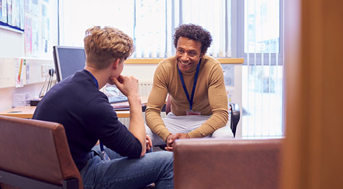 2 people sitting down talking in front of a computer monitor