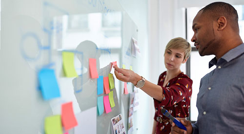 2 people standing in front of a white board with post-it notes scattered across it