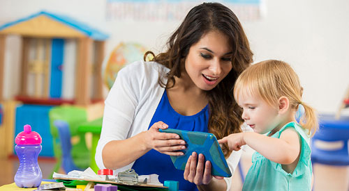 teacher working with a toddler who is pointing at a tablet