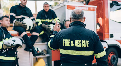 Fire and rescue workers standing in a circle talking next to a firetruck