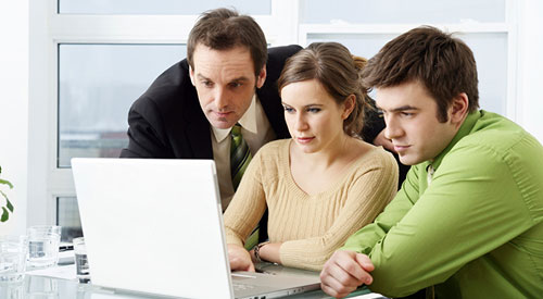 3 people huddled around a laptop sitting on a table