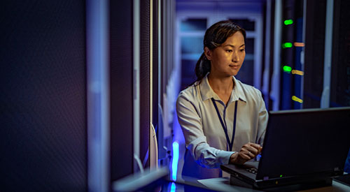 woman sitting in a data center looking at a laptop screen