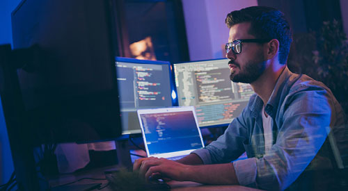 Man sitting in front of multiple computer screens with code on them