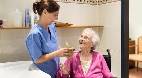 nursing assistant helping with an elderly patient to brush their teeth