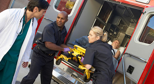 paramedic technicians removing a patient from an ambulance with a doctor waiting