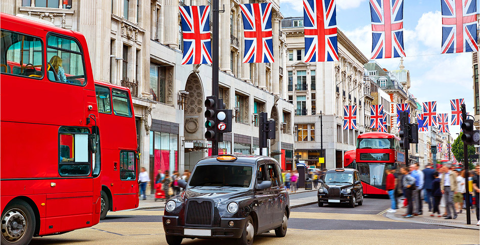 Image of London street with flags and 2 story red busses and people standing at stoplights