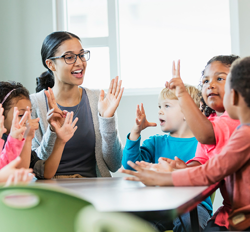 Adult women sitting around a table with children practicing numbers with their hands