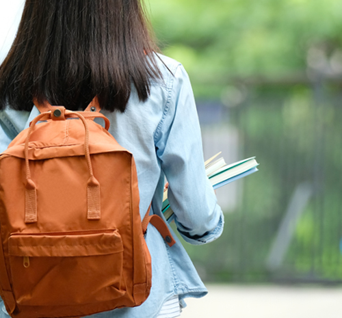 person wearing an orange backpack carrying notebooks