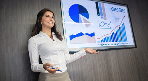 person standing next to a tv with graphs on it presenting information