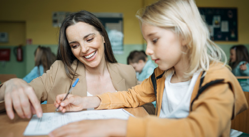 Early childhood education teacher helping student with assignment in classroom