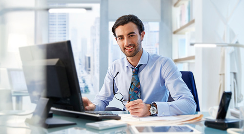 Person sitting in front of a computer at their desk looking at the camera