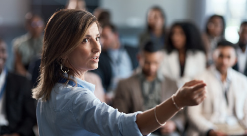 Person presenting in front of a group of people pointing back at a whiteboard