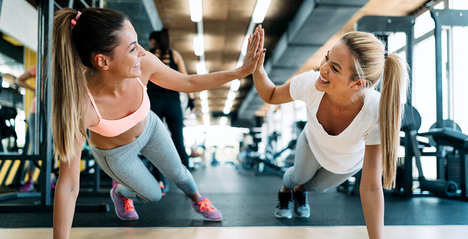 2 people planking giving each other a high five in a gym with weight equipment behind them