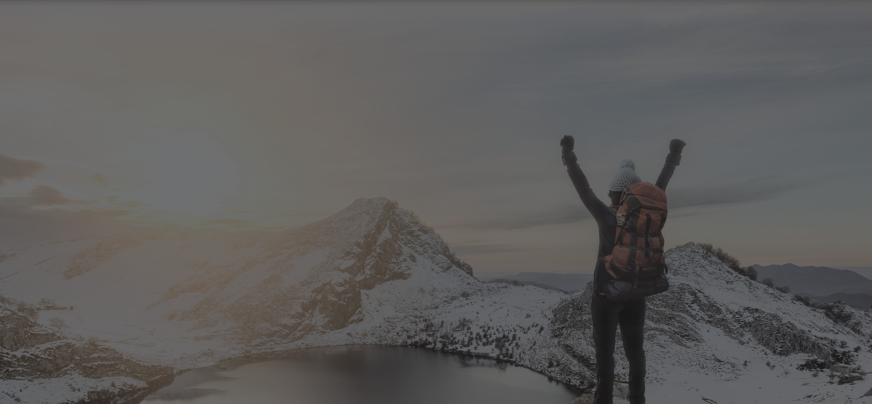 person on snowy mountains with hands in the air overlooking a lake in the middle