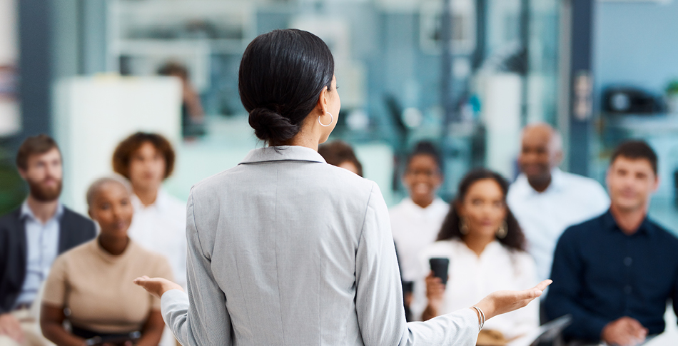 View of the back of a person standing presenting in front of a group of people sitting in front of them