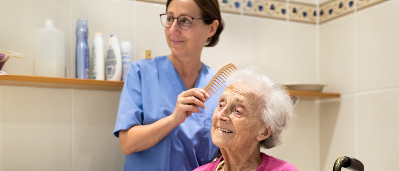 Woman with glasses brushing elderly woman's hair