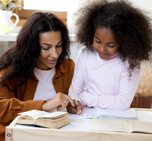 adult and child writing on pad of paper sitting on a coffee table. 2 books are also laying on the table 