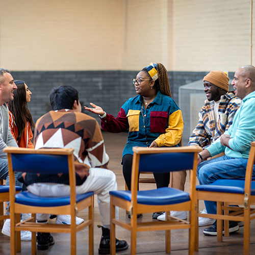 Group of people sitting in chairs arranged in a circle having a discussion.