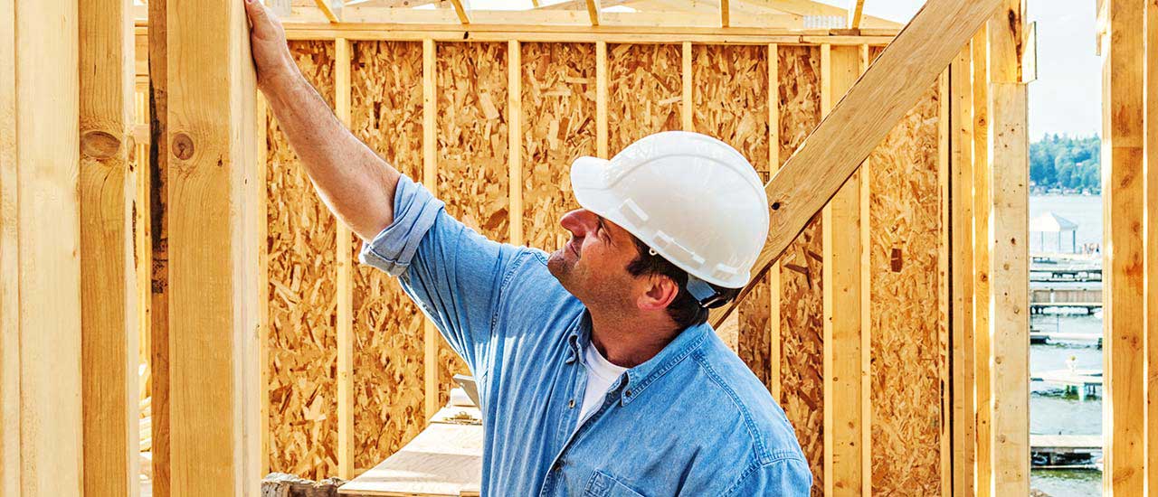 Person wearing a hard hat inspecting a beam inside of a house currently being framed