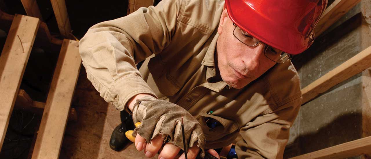 Construction electrician in a hardhat working on electrical inside of a house