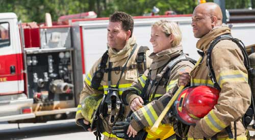 3 FIrefighters standing in full gear next to a firetruck