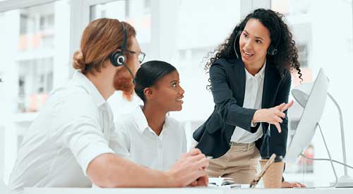 Person standing next to two people sitting at a computer pointing to something on the monitor