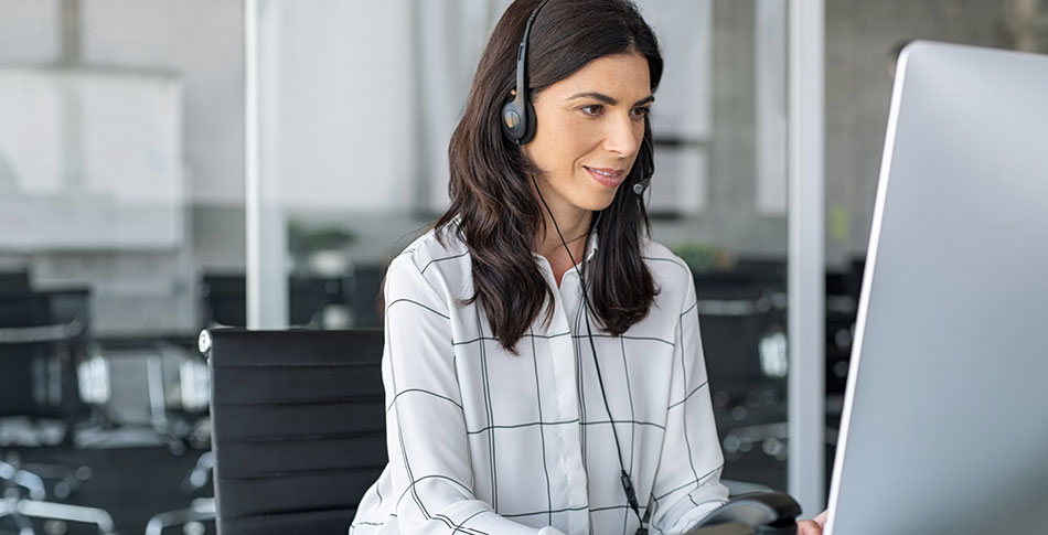 Woman sitting at a computer with a headset on.