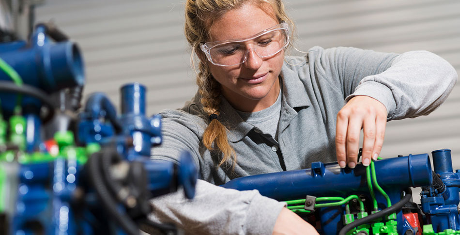 Woman wearing eye protection works on a motor.