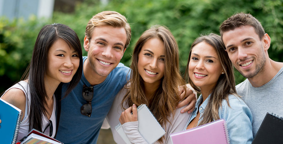 Group of students stand next to each other holding notebooks and smiling.