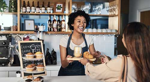 Person working behind a counter handing a pastry and coffee over the counter to a customer