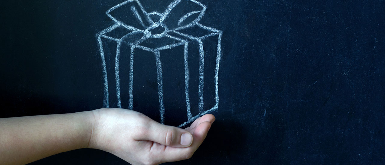 A person's hand underneath a drawing of a present on a chalkboard.
