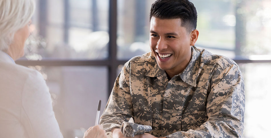 Man in military uniform smiles at someone sitting across from him.