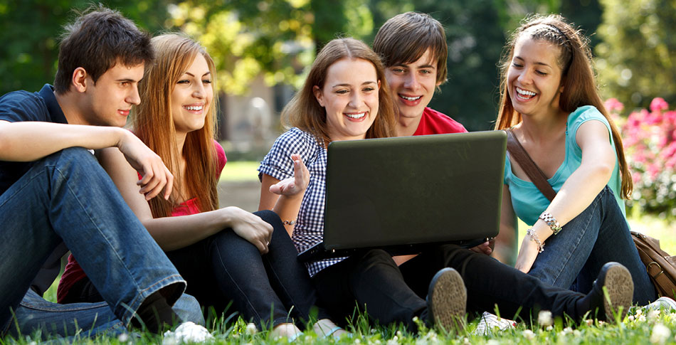 Group of students sit on the grass looking at a laptop.