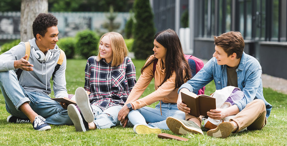 Four students sitting outside in the grass talking.